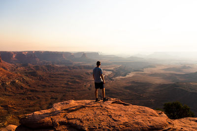 Rear view of man standing on mountain against clear sky