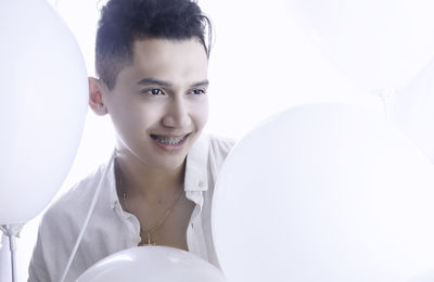 Close-up of smiling young man with balloons against white background