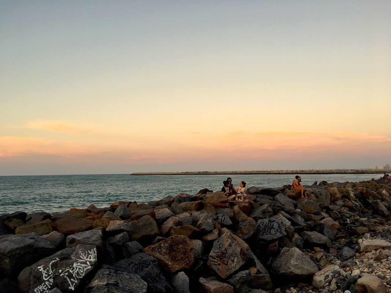 SILHOUETTE PEOPLE STANDING ON ROCK BY SEA AGAINST CLEAR SKY