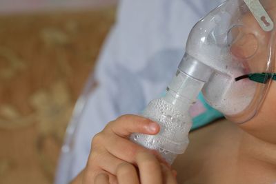 Midsection of patient inhaling through oxygen mask in hospital