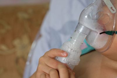 Midsection of patient inhaling through oxygen mask in hospital