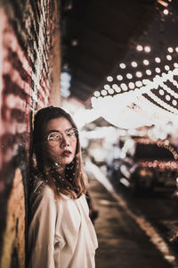 Portrait of beautiful woman against illuminated lights at night