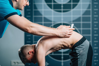 Cropped image of man with male athlete bending in health club