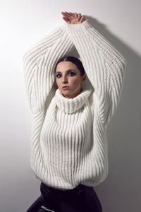 Fashionable girl in a white knitted sweater and leather pants stands on a white background