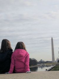 Rear view of girls sitting against sky