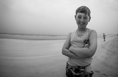 Portrait of smiling boy with arms crossed standing on sand at daytona beach