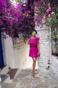 Young beautiful woman in pink dress standing tree with pink flowers in narrow white alley in turkey