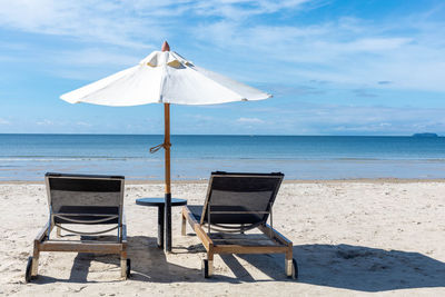 Deck chairs on beach against sky