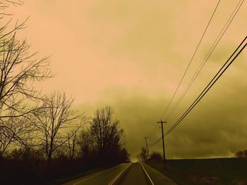 Road by trees against sky during sunset