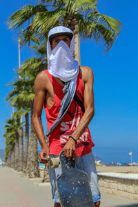 Midsection of man with palm trees on beach against clear blue sky