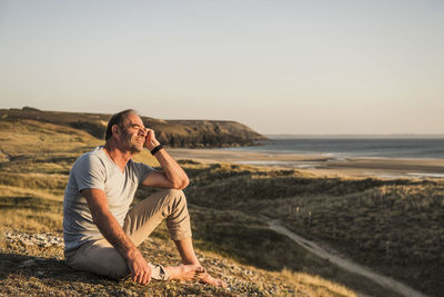 Thoughtful mature man sitting with head in hand on hill