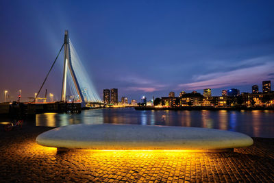Illuminated city by river against sky at dusk