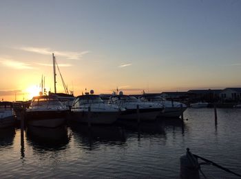 Sailboats moored in harbor at sunset