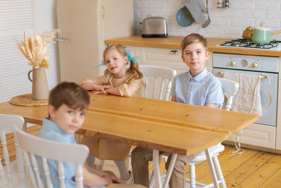 Children sit at table in kitchen and wait for their parents to make them