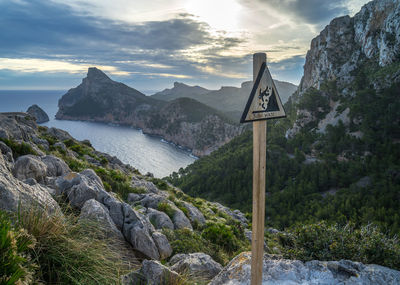 Warning sign on rock against mountains during sunset