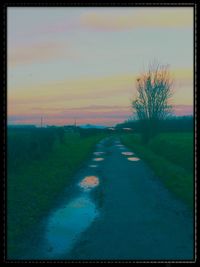 Road amidst field against sky during sunset