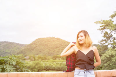 Portrait of smiling young woman standing against sky