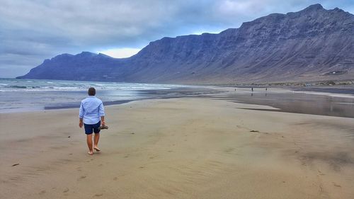 Rear view of man walking at beach against rocky mountains
