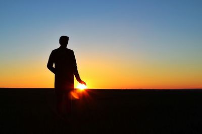 Silhouette man standing on field against clear sky during sunset