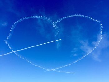 Low angle view of heart shape vapor trail against blue sky