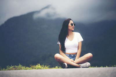 Young woman looking away sitting against mountain