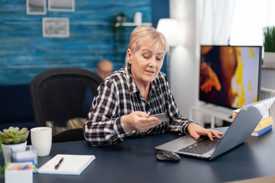 Senior woman holding credit card while using laptop at office