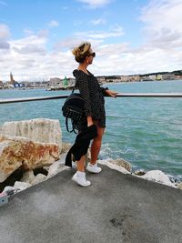 Woman standing on retaining wall by sea against sky