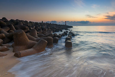 Rocks in sea against sky during sunset