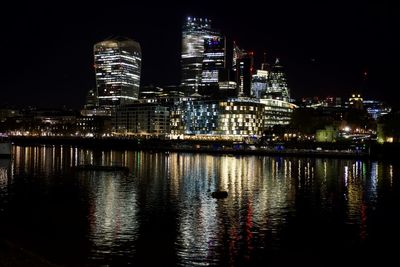 Illuminated buildings by river against sky at night
