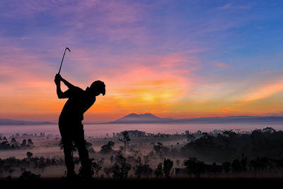 Silhouette man playing golf on field against sky during sunset