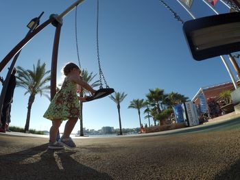 Low angle view of girl playing on swing against clear sky