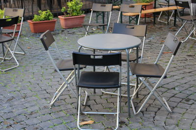 Empty chairs and tables at sidewalk cafe amidst buildings