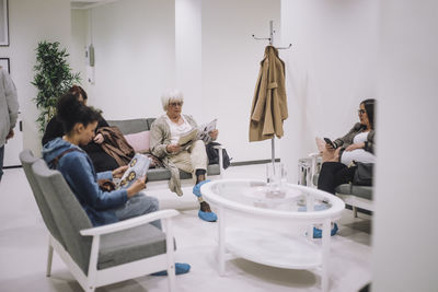 Female patients reading magazines while sitting in waiting room at hospital