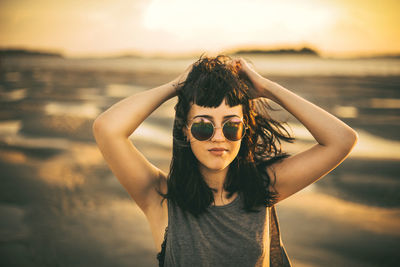 Portrait of young woman standing at beach during sunset