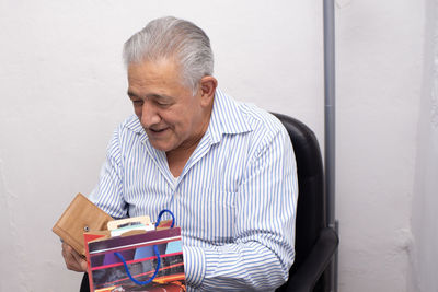 Older man opening gift, talking and celebrating birthday indoors, old birthday