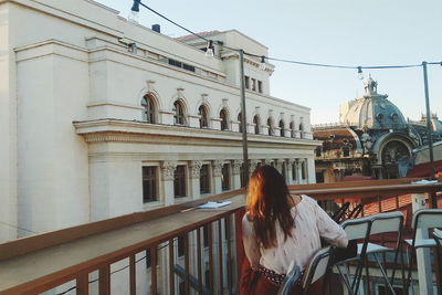 Rear view of woman sitting on chair at building terrace in city