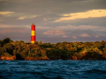 Lighthouse amidst sea and buildings against sky