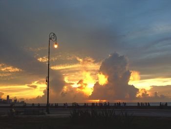 Silhouette street lights on beach against orange sky