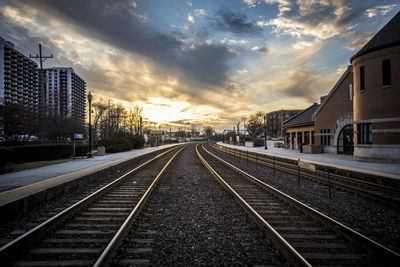 Railroad tracks amidst buildings against sky during sunset