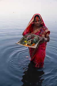 Woman holding red umbrella standing in lake