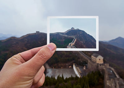 Close-up of hand holding photograph against mountain