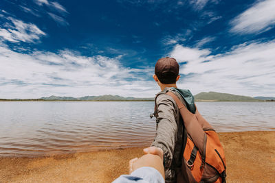 Man holding hand while standing at sea shore against sky