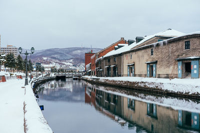 Buildings by canal against sky in city during winter