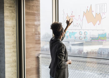 Young woman touching windowpane with graph in office