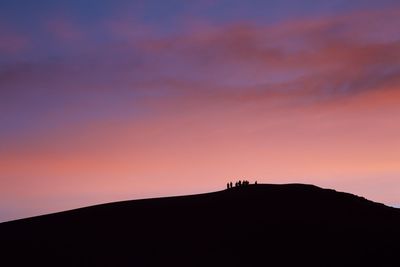 Silhouette people on mountain against sky during sunset