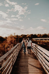 Rear view of people walking on footbridge against sky