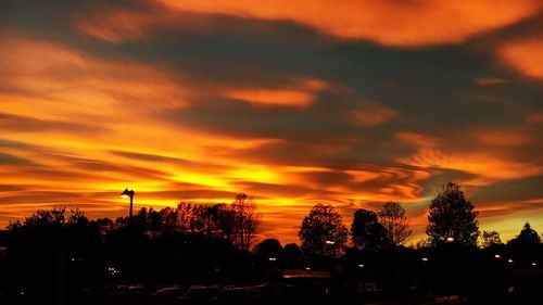 Silhouette trees against dramatic sky during sunset