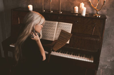 High angle of woman looking at music note while playing piano