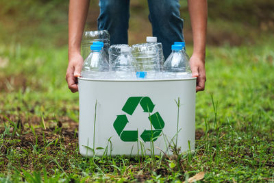 A woman holding a recycle bin with plastic bottles in the outdoors