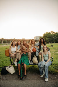 Multiracial teenage girls sitting on bench at park during sunset